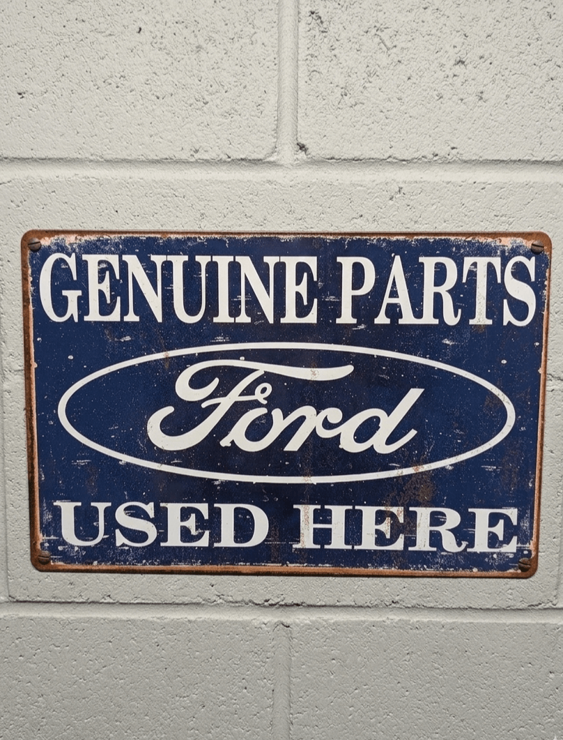 Vintage-style navy blue metal wall sign with white text saying Genuine Parts Ford Used Here, featuring a heavily distressed and rusted effect for garage decor