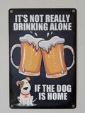Vertical vintage-style metal wall sign with the text 'IT'S NOT REALLY DRINKING ALONE IF THE DOG IS HOME' in bold white letters, featuring an illustration of two clinking beer mugs and a small, happy dog at the bottom on a distressed dark blue background.
