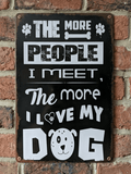 Vintage-style vertical black metal wall sign featuring bold white typography that reads 'The More People I Meet, The More I Love My Dog' with paw prints and a cute dog face illustration.