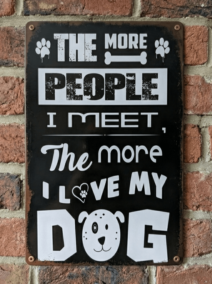 Vintage-style vertical black metal wall sign featuring bold white typography that reads 'The More People I Meet, The More I Love My Dog' with paw prints and a cute dog face illustration.