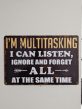 Horizontal vintage-style metal wall sign with the text 'I'M MULTITASKING I CAN LISTEN, IGNORE AND FORGET ALL AT THE SAME TIME' in yellow and white typography on a dark, distressed background with rusted edges