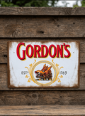Vintage-style landscape metal wall sign for Gordon's London Dry Gin, featuring the iconic red brand name and the golden wild boar crest with 'ESTD 1769' on a distressed white background with rusted edges