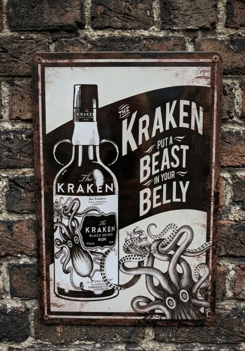 Vertical vintage-style metal wall sign for The Kraken Black Spiced Rum, featuring a detailed illustration of a kraken attacking a ship next to a bottle with the slogan 'Put a Beast in your Belly' on a distressed white and dark brown background.
