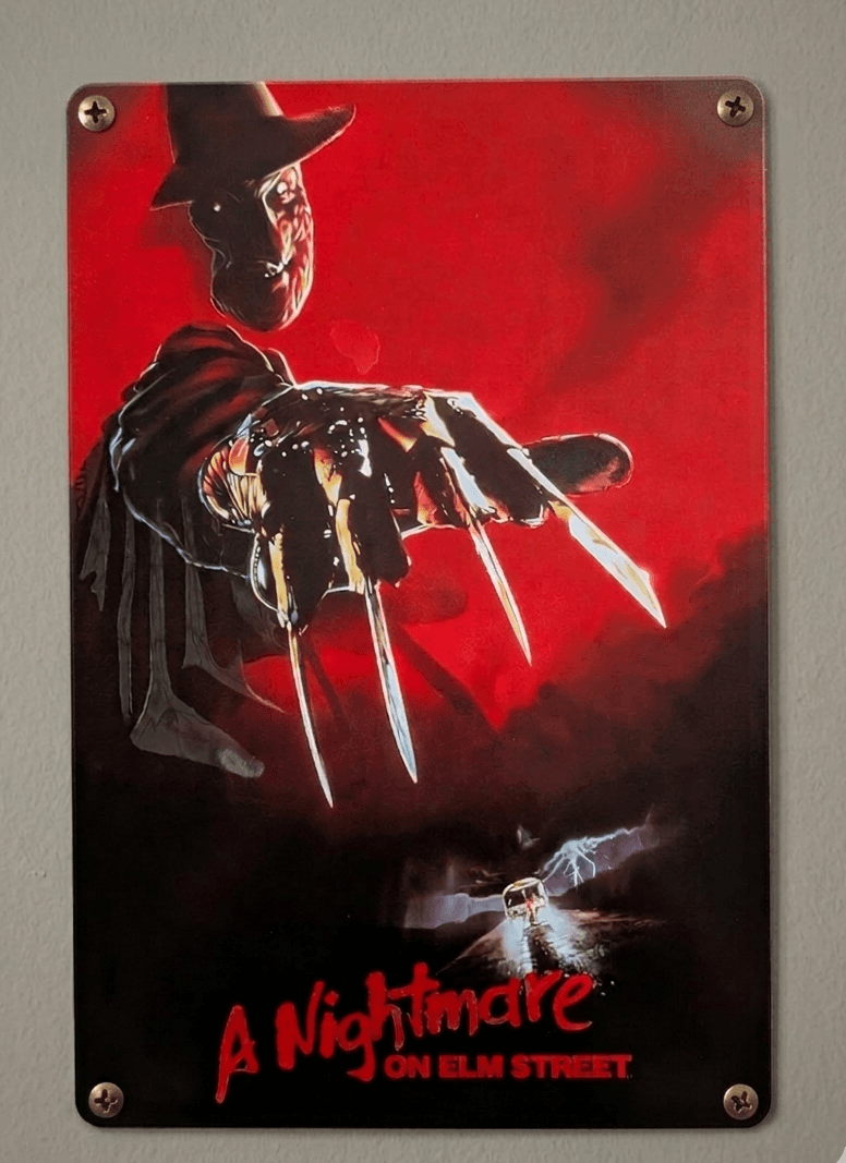 Vertical metal wall sign for A Nightmare on Elm Street, featuring Freddy Krueger’s razor-gloved hand reaching out over a dark road with a lone car under a red and black sky.
