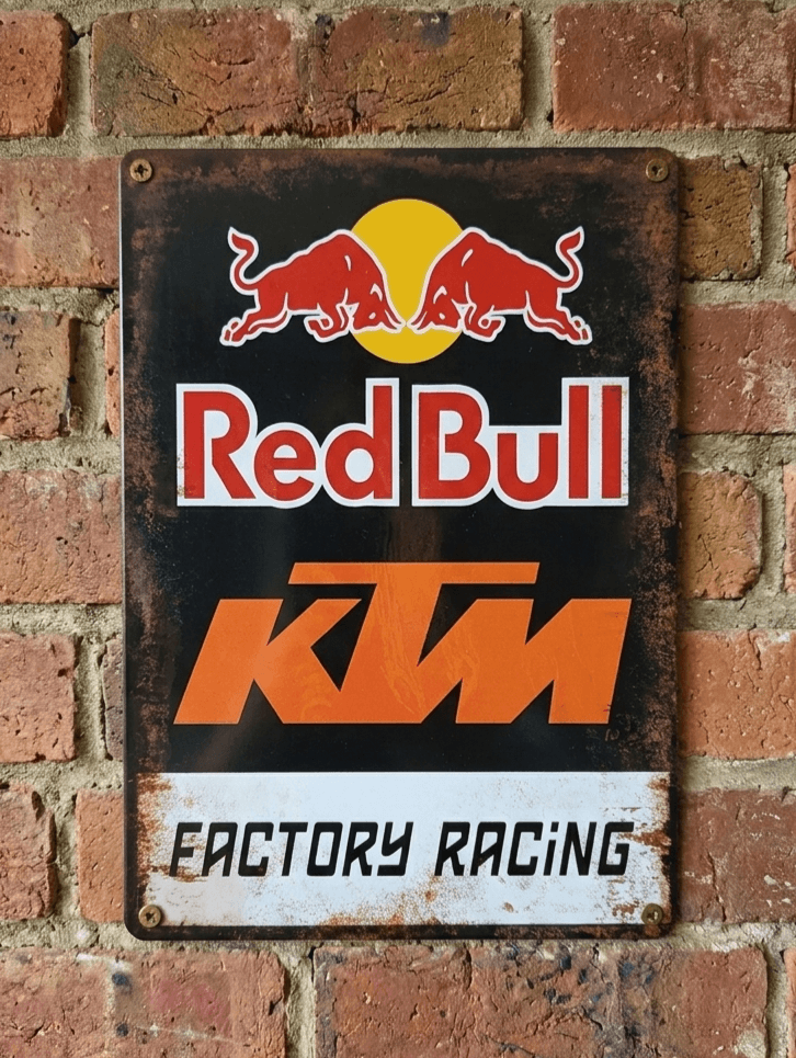 Vintage-style metal wall sign featuring the Red Bull logo and KTM Factory Racing branding with a heavily distressed, rusted border on a brick background
