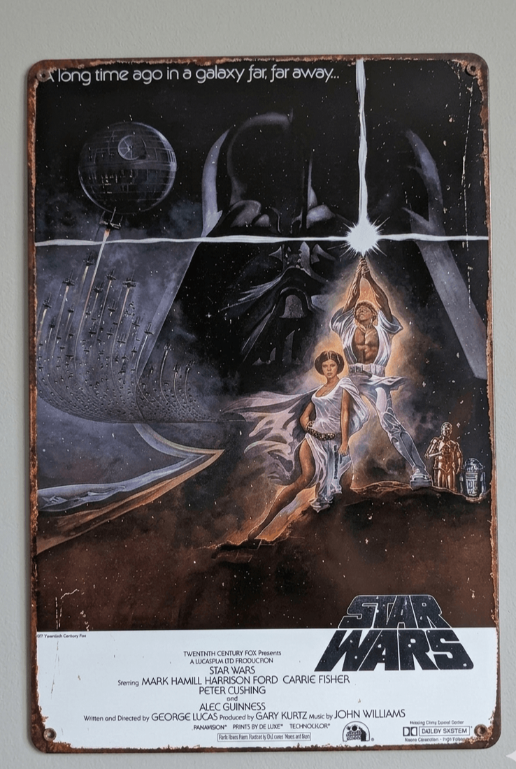 Vertical metal wall sign featuring the original 1977 Star Wars movie poster art with Luke Skywalker holding a lightsaber aloft, Princess Leia, Darth Vader's mask in the background, and the Death Star.