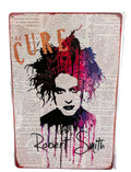 Vertical retro-style metal wall sign featuring a colorful splash watercolor portrait of Robert Smith from The Cure over a printed background of vintage dictionary text, complete with his signature script and distressed rusted edges.