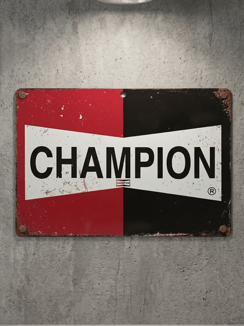Horizontal vintage-style metal wall sign for Champion Spark Plugs, featuring a split red and black background with the iconic white bow-tie logo and 'CHAMPION' in bold black text, mounted on a grey concrete wall with rusted edges.