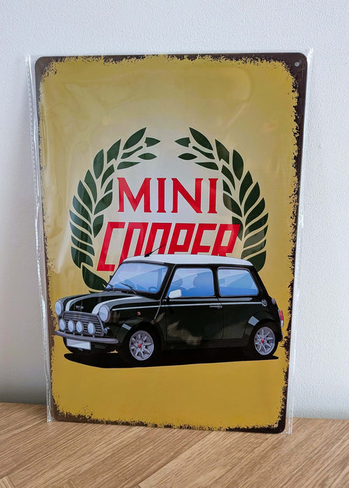 Vertical vintage-style metal wall sign for Mini Cooper in protective plastic wrap, featuring an illustration of a classic dark green Mini with a white roof in front of a green laurel wreath logo on a distressed yellow background with heavily rusted borders.