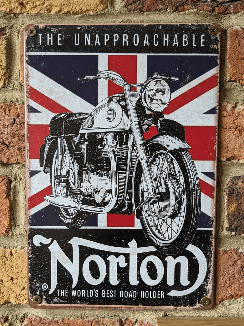 Vertical vintage-style metal wall sign for Norton Motorcycles, featuring a detailed black and white illustration of a classic bike over a distressed Union Jack flag, with 'The Unapproachable' and 'The World's Best Road Holder' text, mounted on a brick wall.